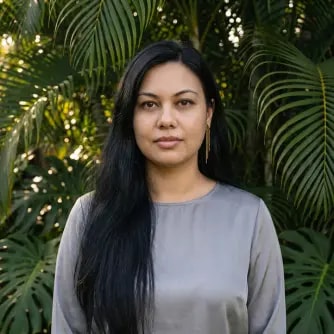 A woman with long black hair standing in front of trees