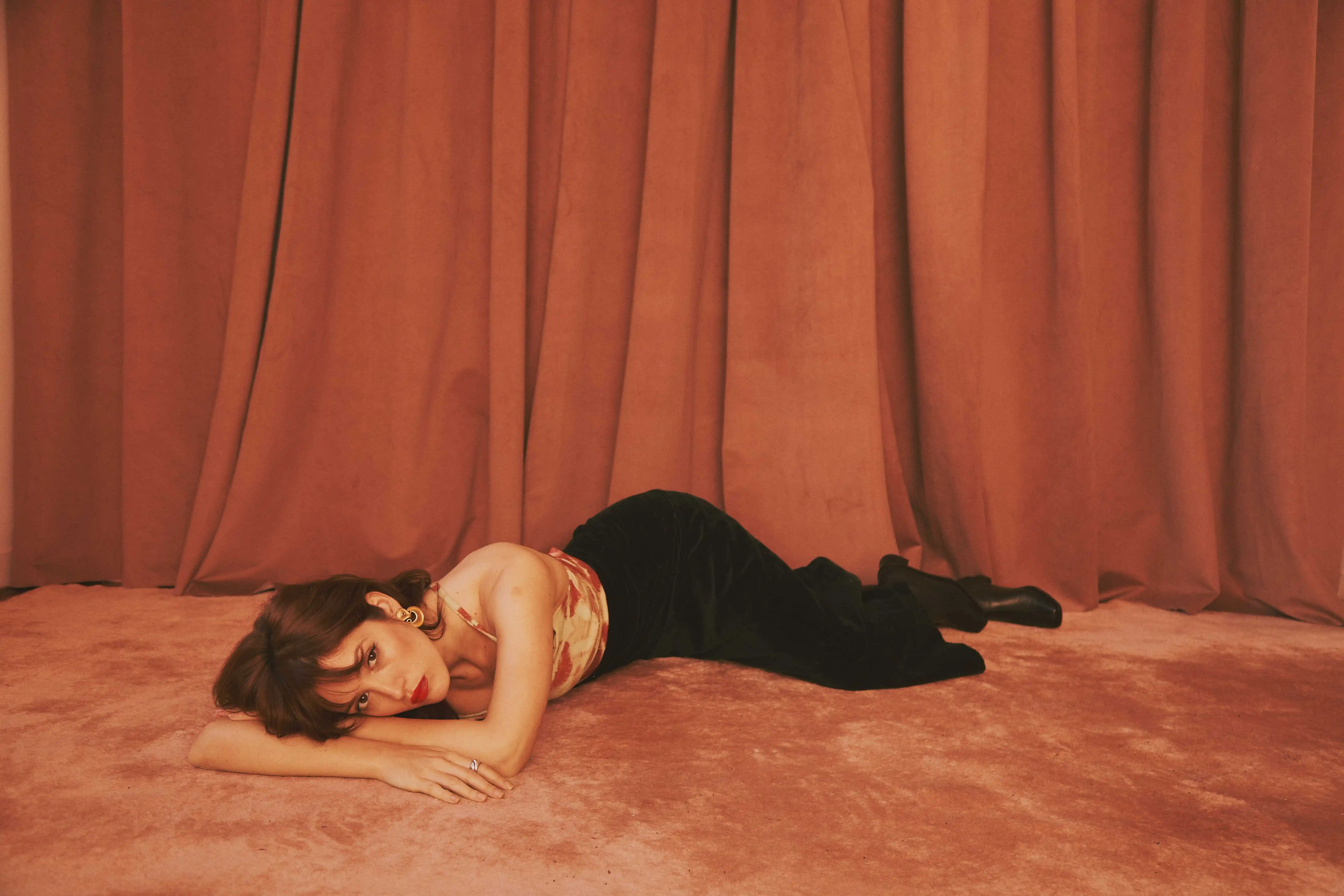A woman laying on the floor in front of a curtain