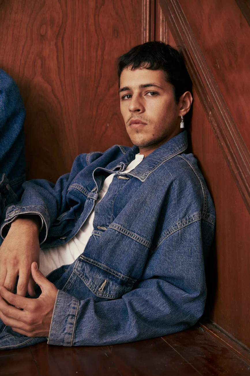 A young man sitting on the floor wearing a jean jacket
