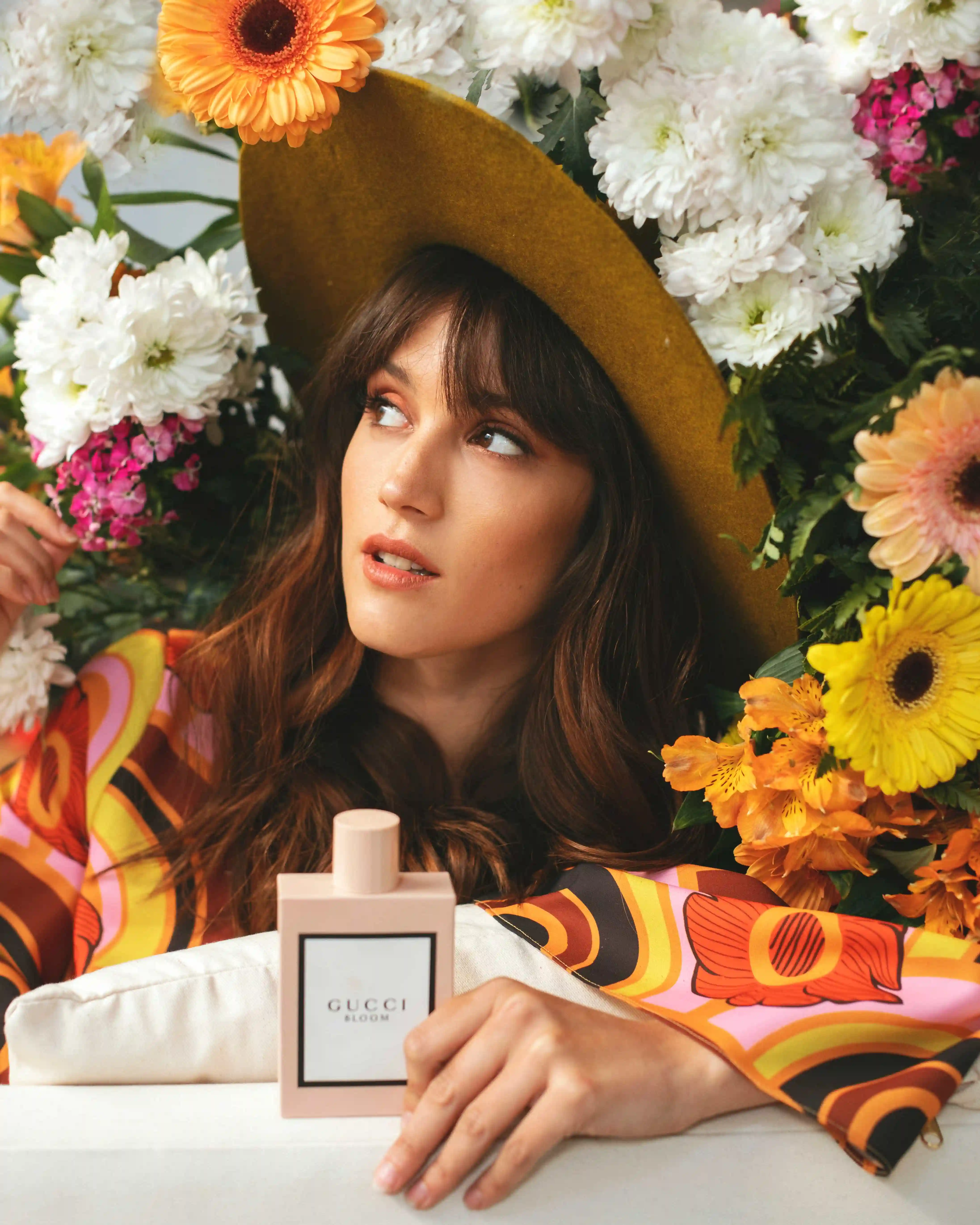 A woman wearing a hat and holding a bottle of perfume