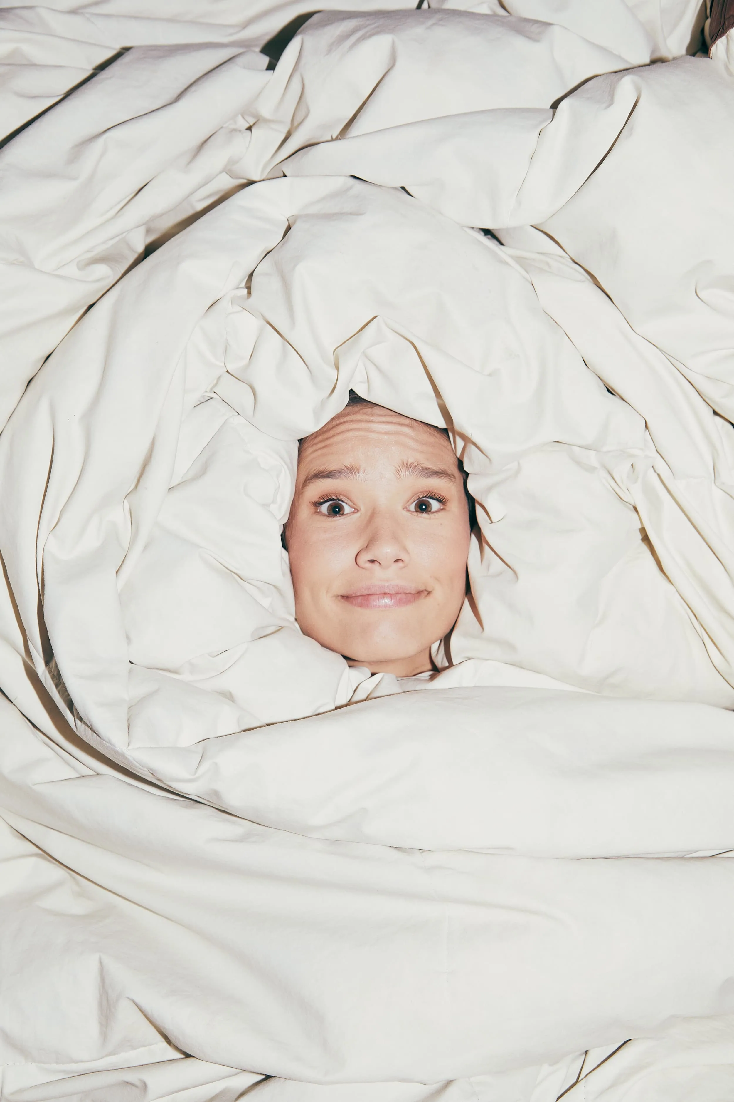 A woman is hiding under a white blanket