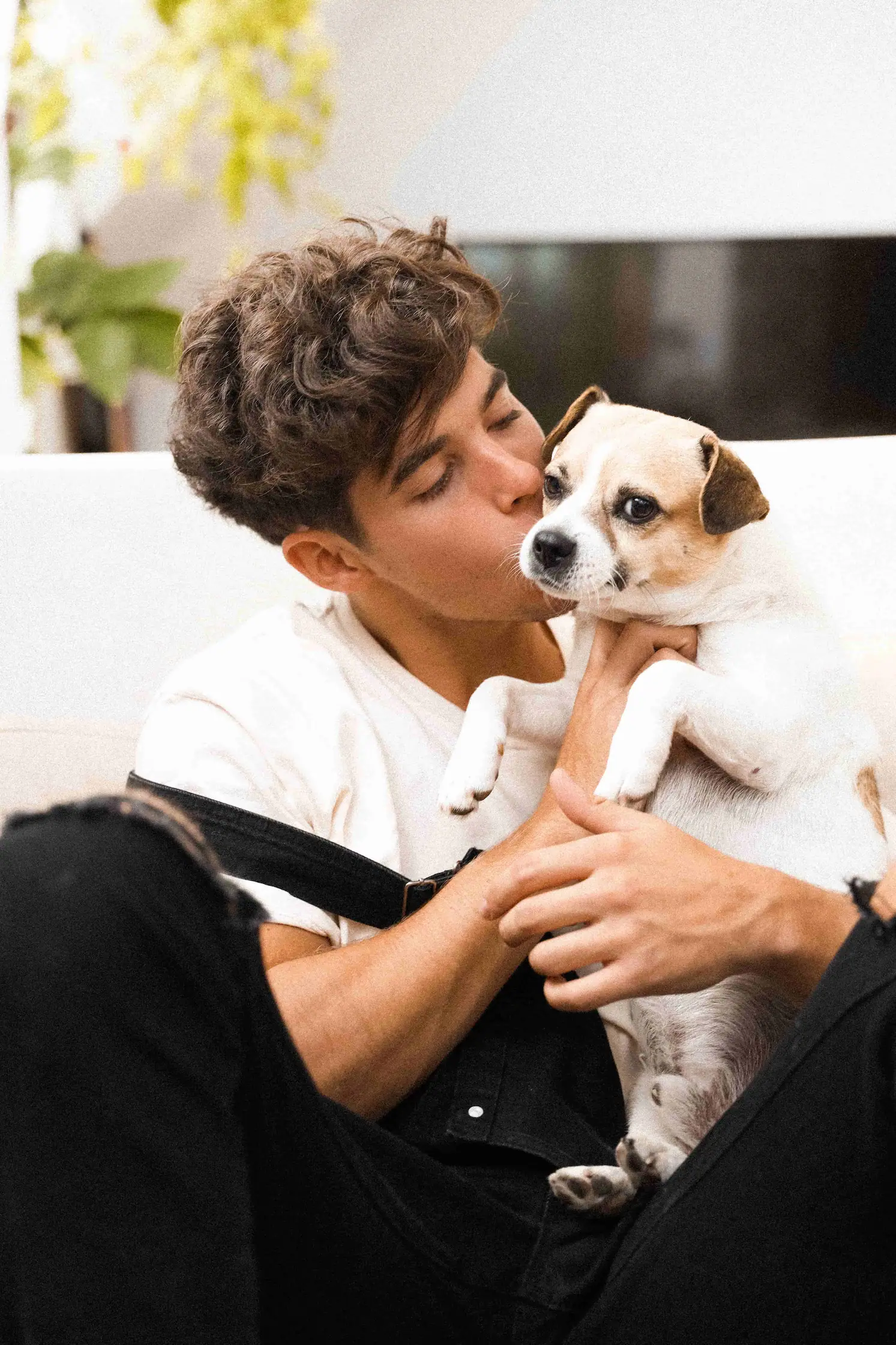 A man sitting on a couch kissing a small dog