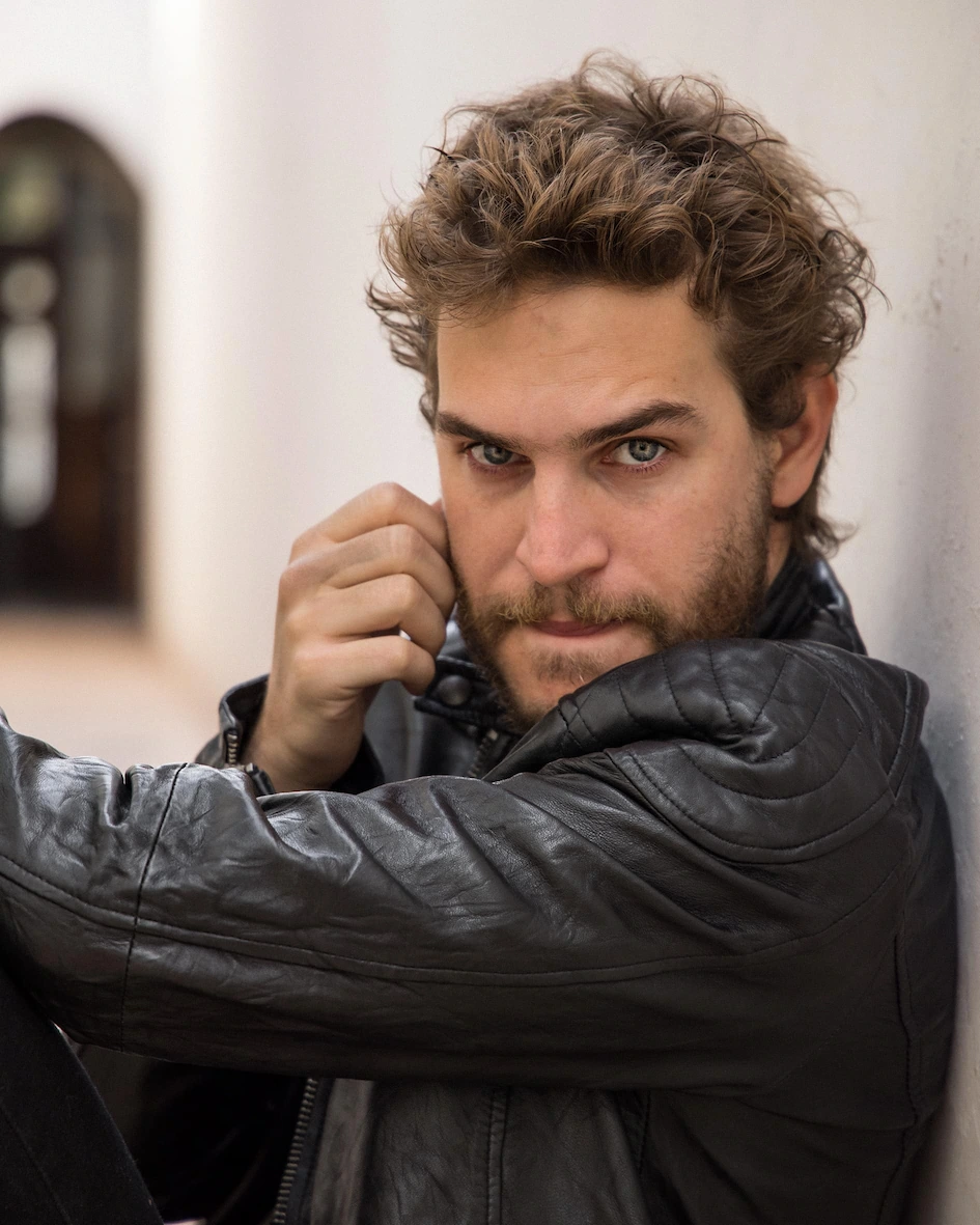 A man leaning against a wall wearing a leather jacket