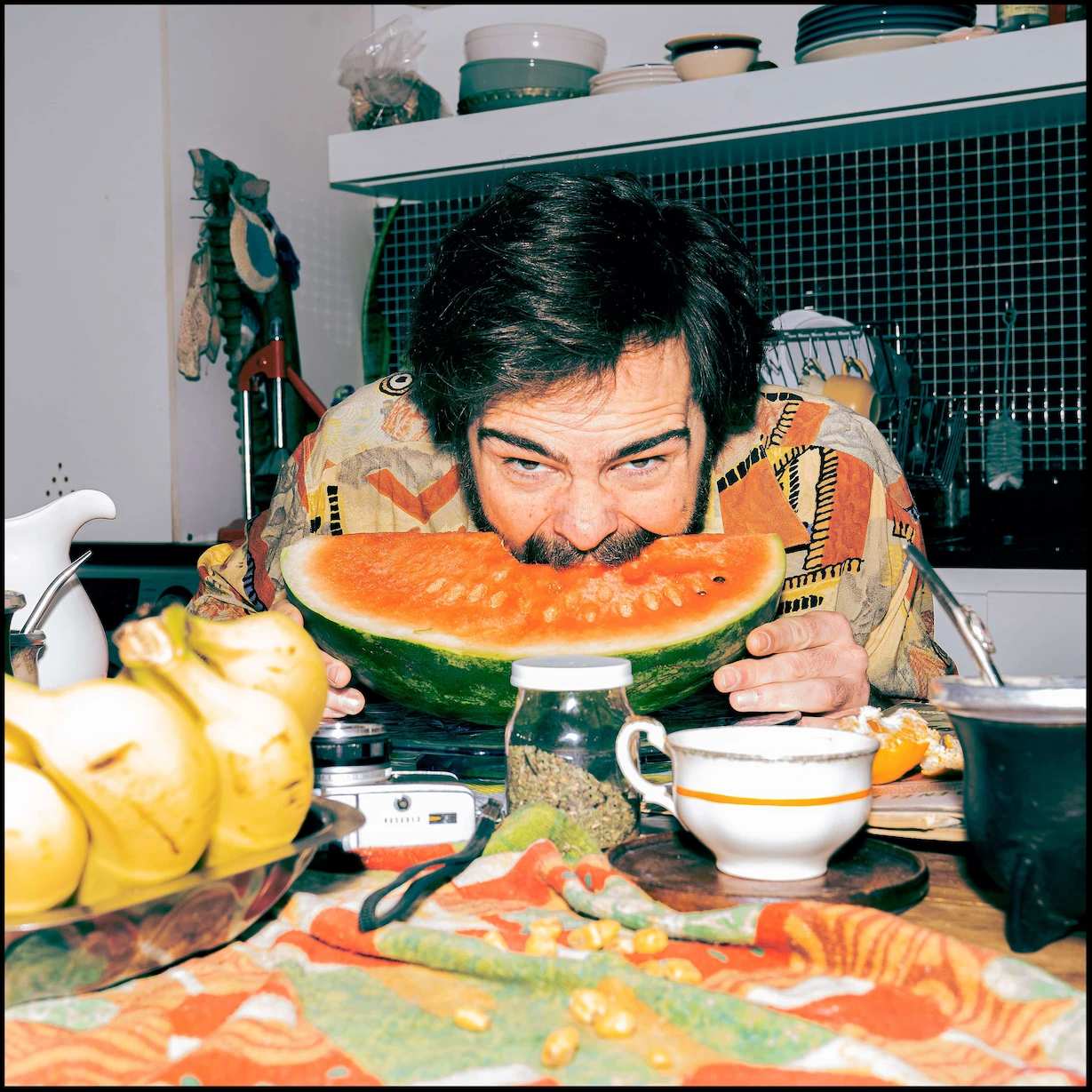A man sitting at a table with a slice of watermelon in front of