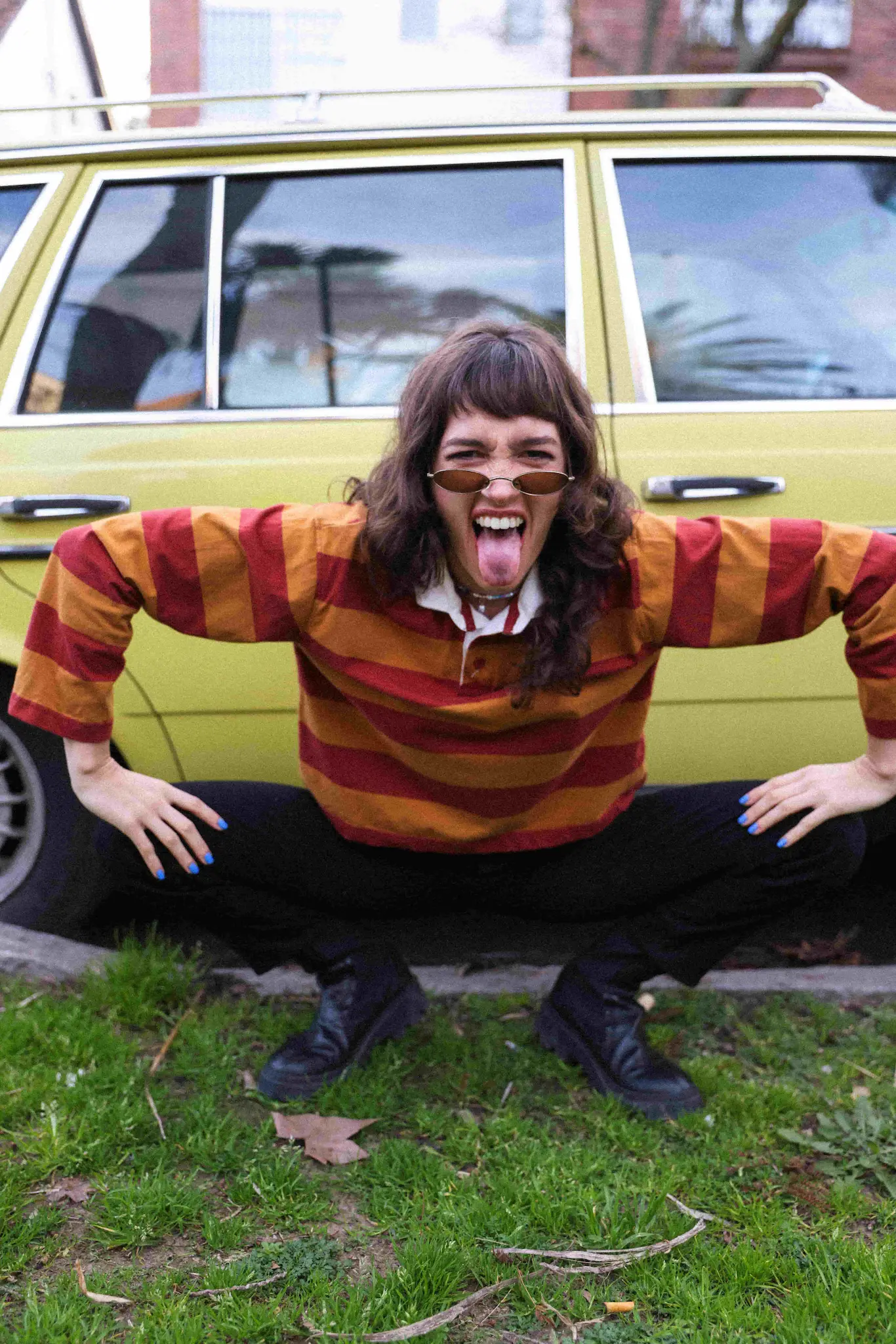 A man with long hair and glasses posing in front of a car