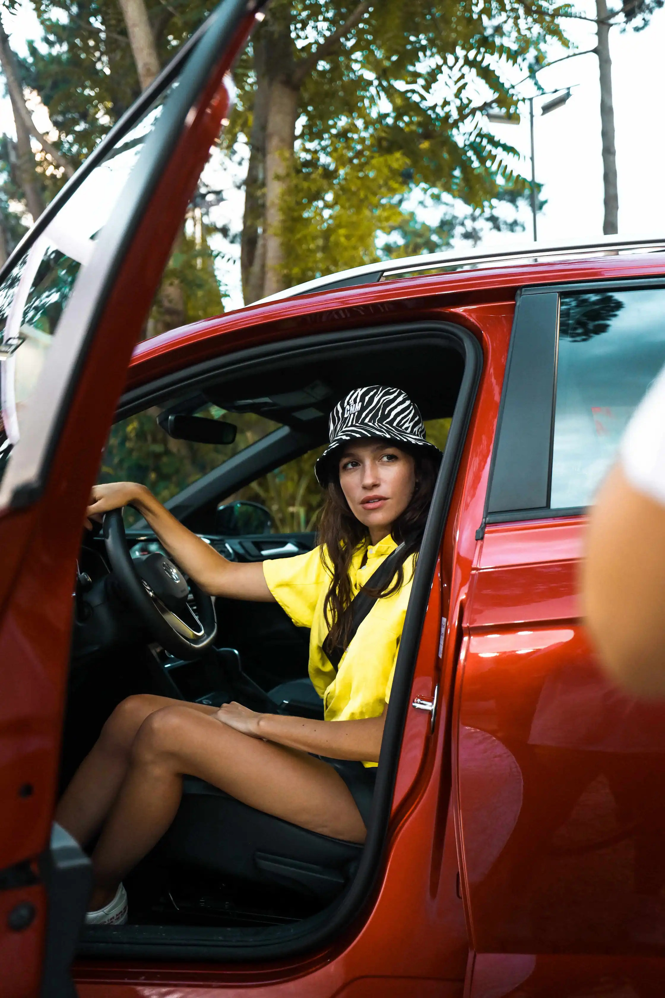 A woman sitting in a red car wearing a hat