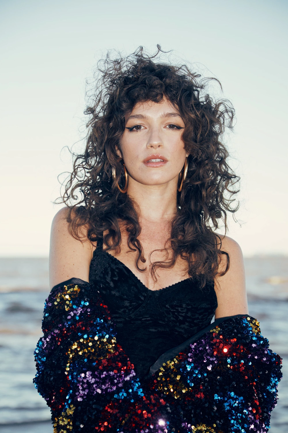 A woman with long curly hair standing in front of the ocean