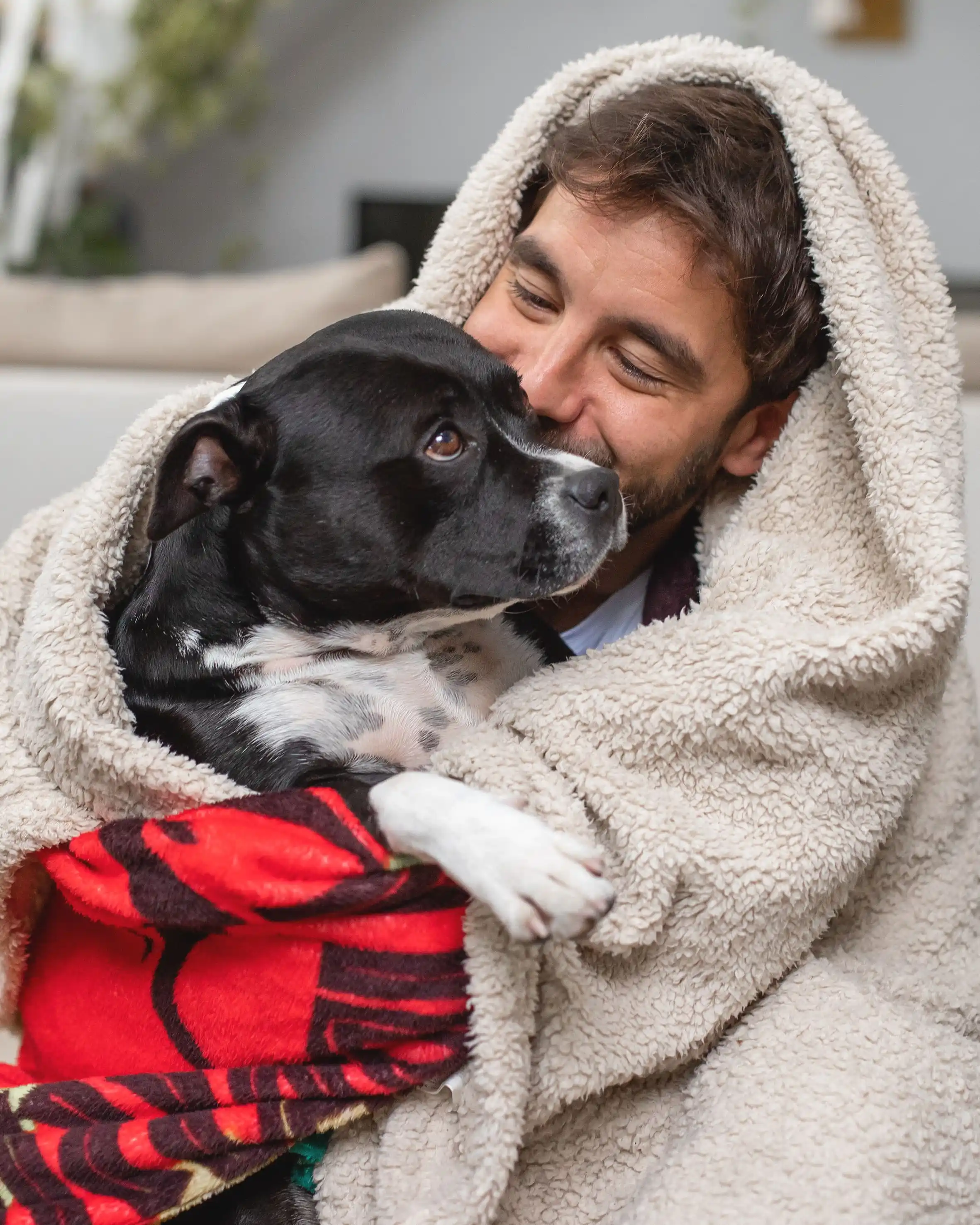 A man wrapped in a blanket hugging a dog