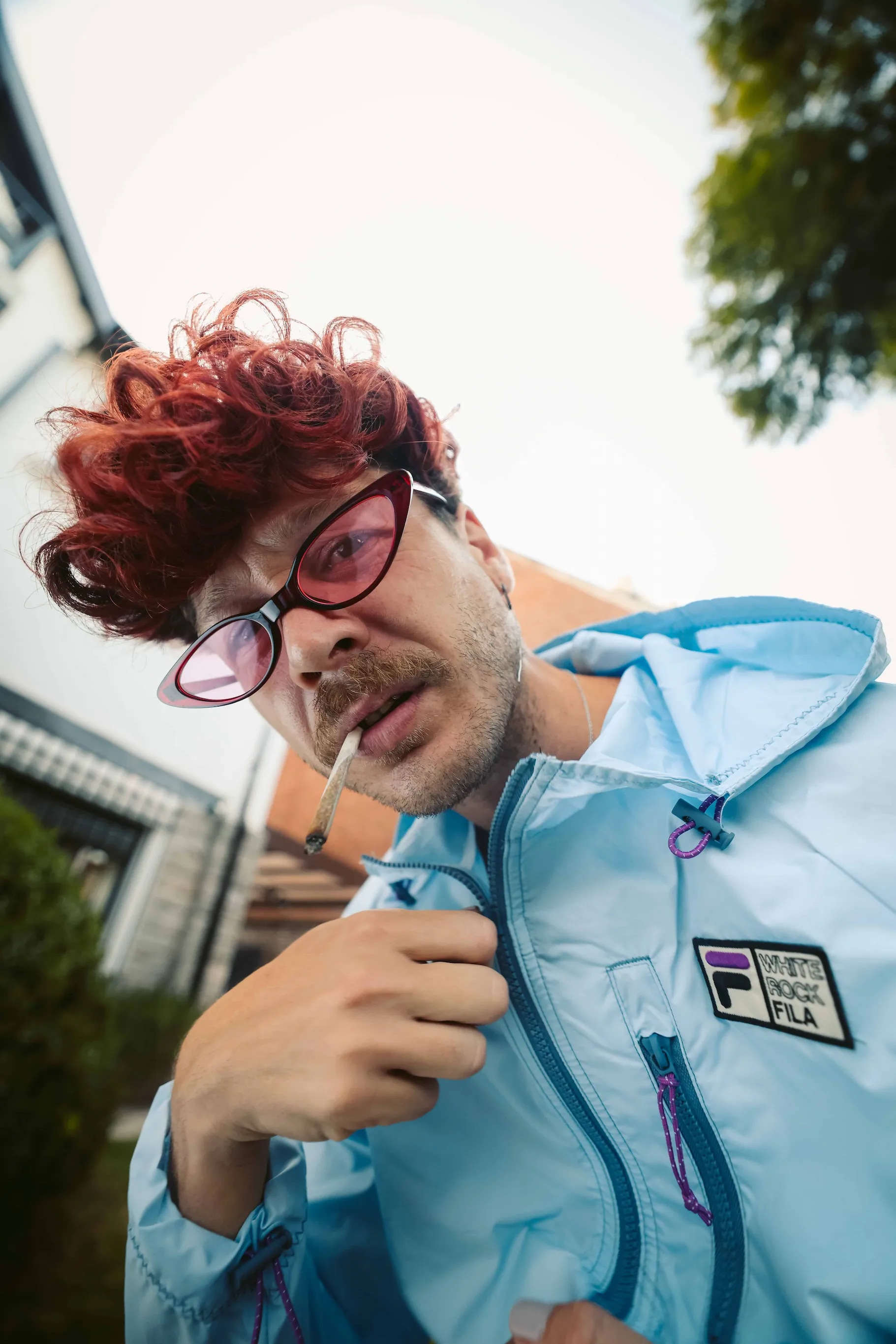 A man with red hair and glasses smoking a cigarette