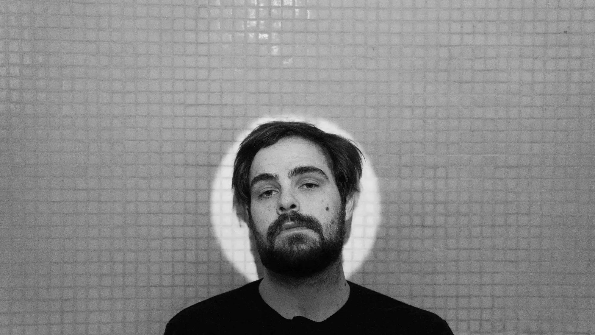 A man with a beard standing in front of a tiled wall