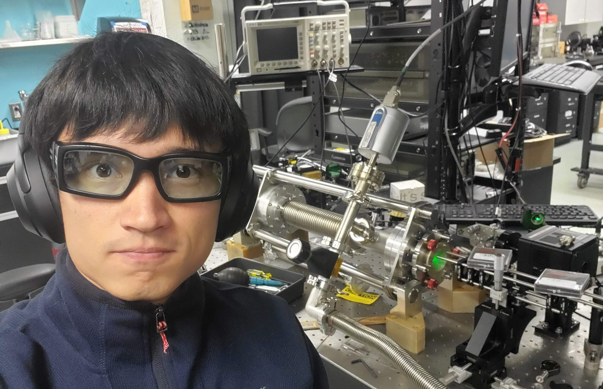 A man wearing glasses and headphones in front of QCL pumped terahertz laser experimental setup at Harvard University